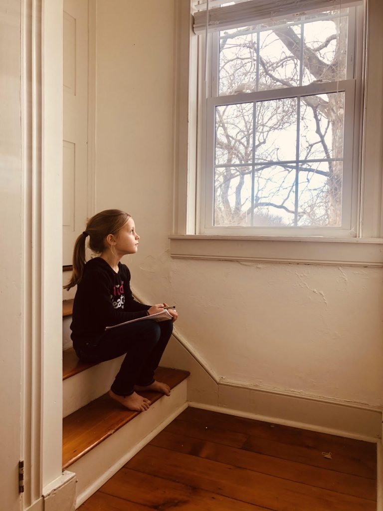 girl looking out the window with notebook and pencil
